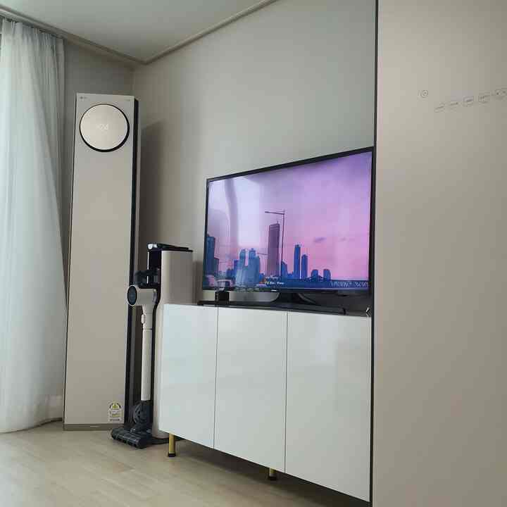 A modern living room in white and beige tones featuring LG Objet collection air conditioner, cordless vacuum, and sleek TV stand