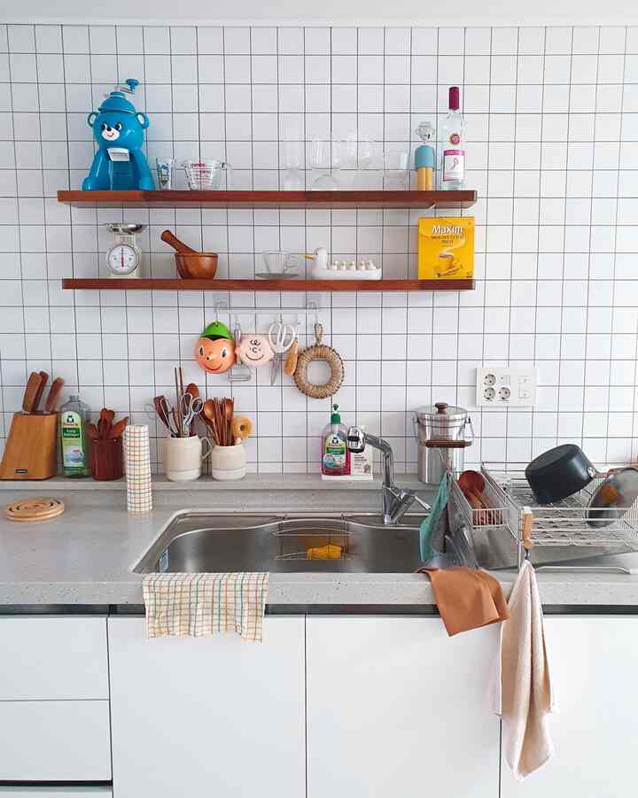 White and natural wood tone kitchen featuring a sink and open shelves neatly arranged with kitchen utensils, creating a practical space