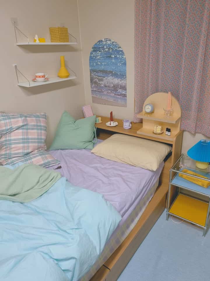 Pastel-toned small bedroom featuring a bed, storage shelves, and pink patterned curtains creating a cozy atmosphere