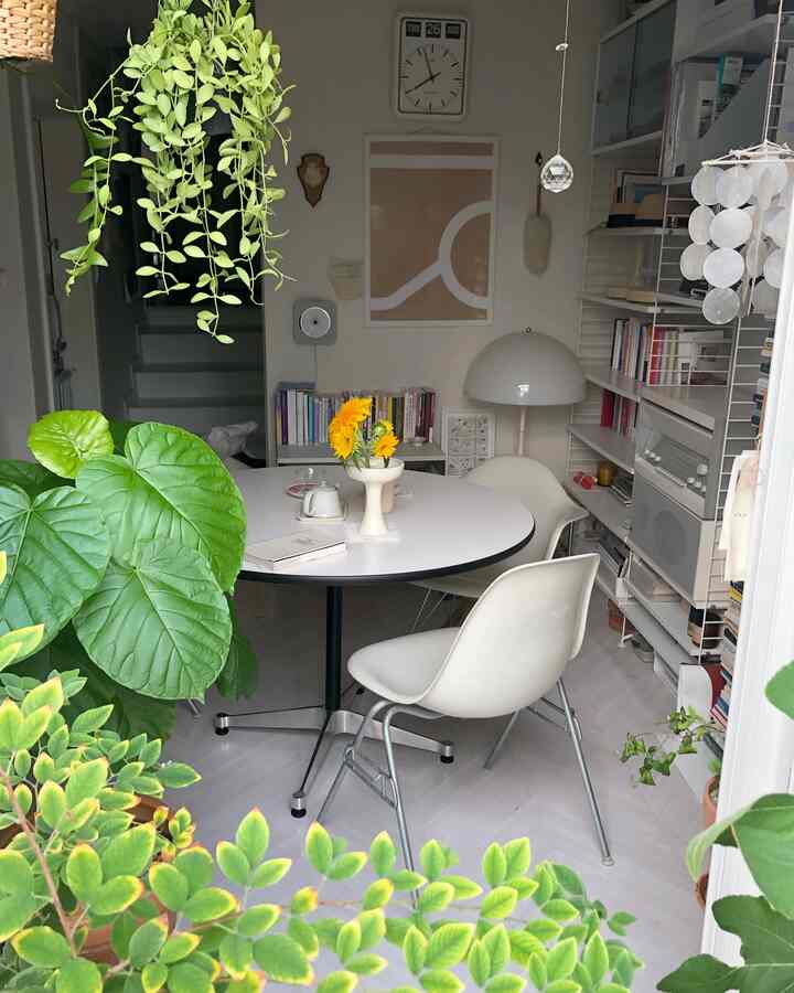 White-toned veranda and living room featuring lush green plants, round dining table, and simple chairs creating a natural atmosphere