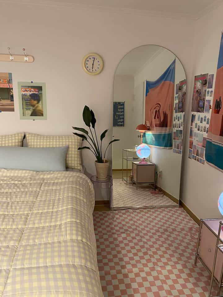 Bedroom featuring pink checkered rug and yellow gingham bedding, with an arch-shaped full-length mirror and a potted plant in a cozy setting