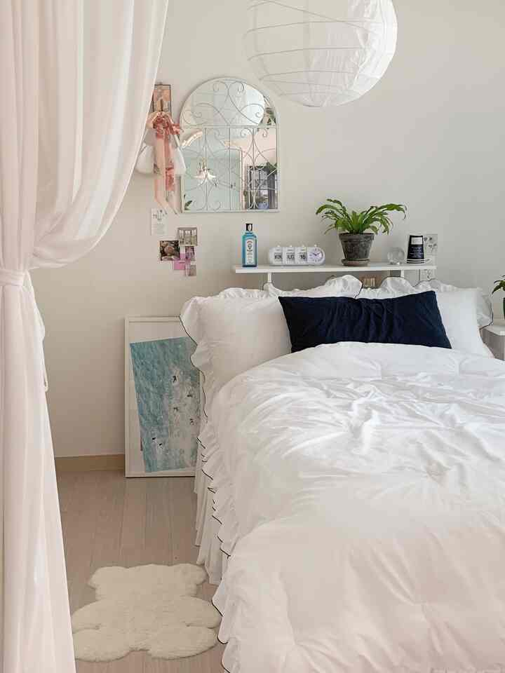 White toned bedroom featuring ruffled bedding, curtain, and plants creating a clean and cozy space