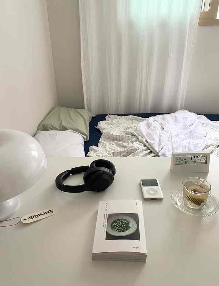 White and navy toned bedroom featuring a simple desk with headphones, book, and coffee cup, creating a cozy atmosphere