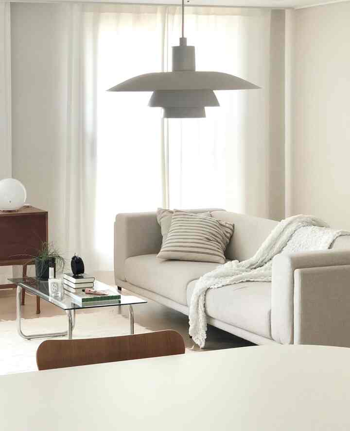 Bright white and beige toned living room featuring a beige sofa and a glass coffee table centrally placed with a clean, natural style
