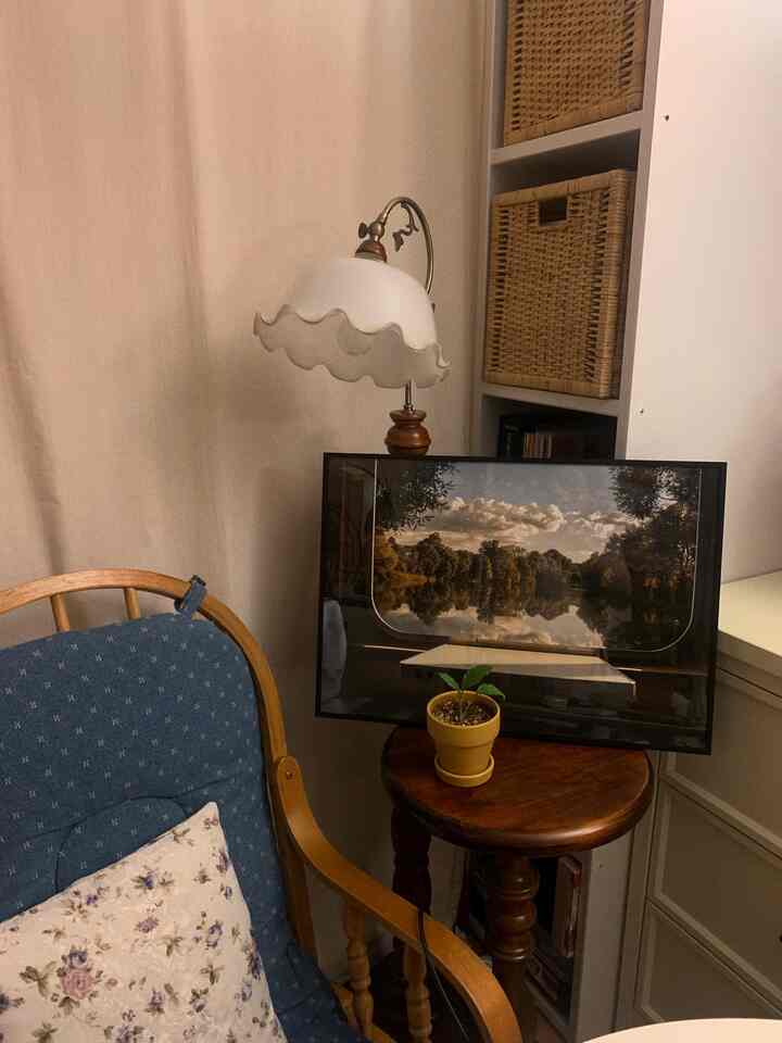 Cozy living room corner with vintage rocking chair in warm brown wood tone and blue cushion, featuring a table lamp and poster