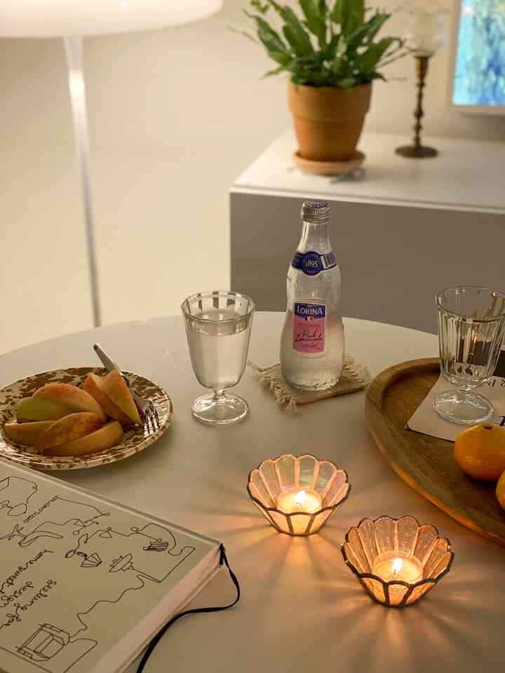 A white-toned table featuring lit candle holders, plates, and glasses creating a cozy, natural atmosphere