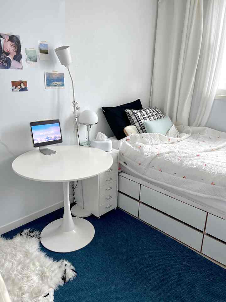 白とネイビーカラーの寝室、ホワイトの丸テーブルと簡易デスクが配置された落ち着いた個人空間