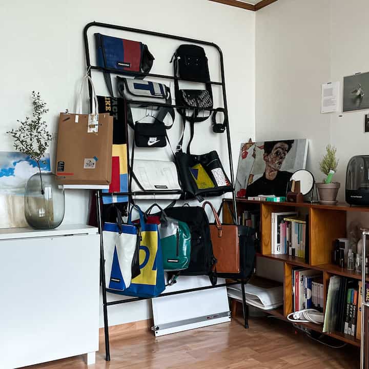 A clean organized space featuring a black metal bag hanger and wooden bookshelf against white walls and brown wooden floor