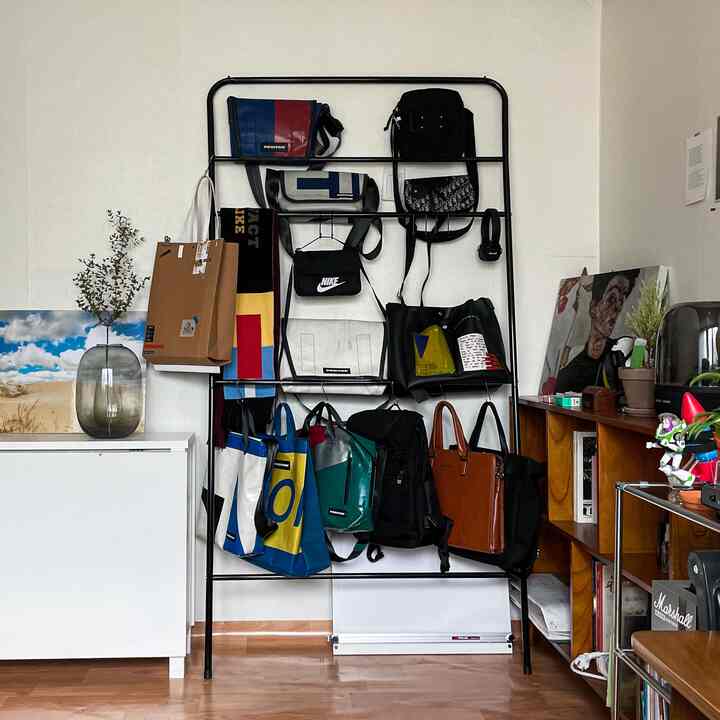 ナチュラルカラーの木目調床と白い収納家具の隣に黒い金属ラックがあり、カラフルなバッグが掛けられた整理された収納アイデアのある空間