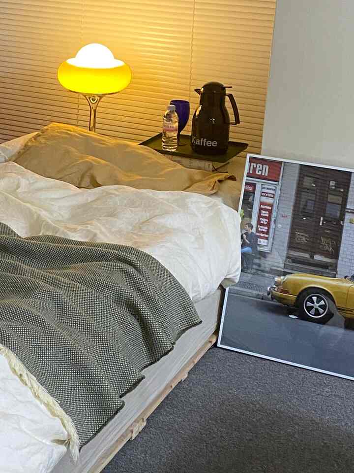 A cozy bedroom with soft natural tones, featuring beige and white duvet covers, blinds, and warm ambient lighting