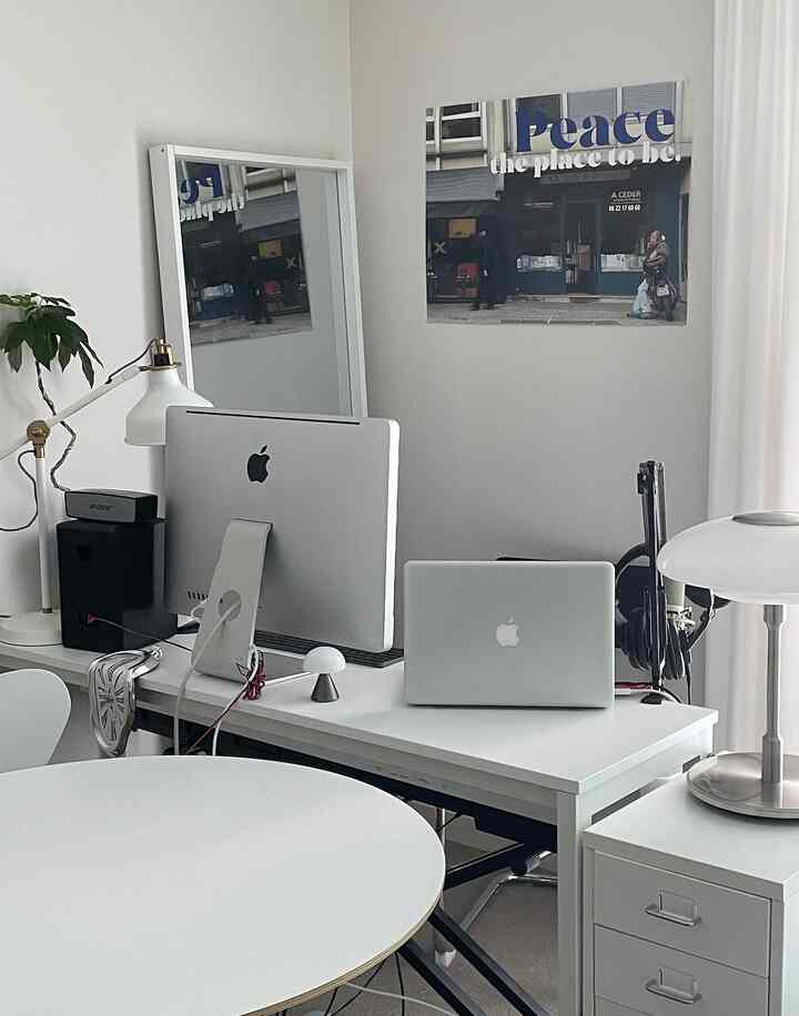 White-toned home office featuring an iMac and MacBook on a simple modern desk with a poster, showcasing a clean workspace