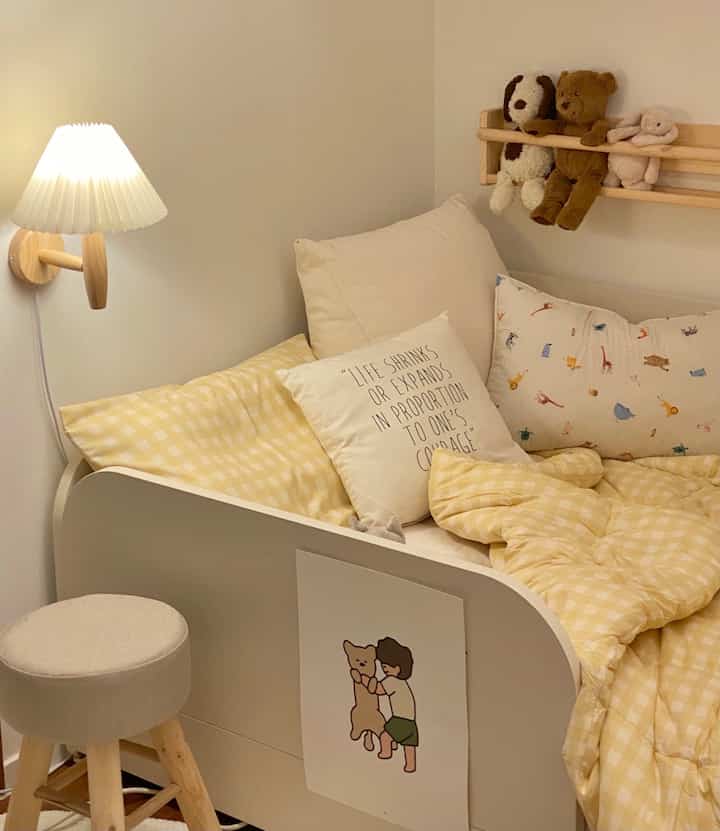 黄色い寝具と白い壁が映える自然な雰囲気の子供部屋、スツールと壁掛け照明がアクセントの温かみあるインテリア