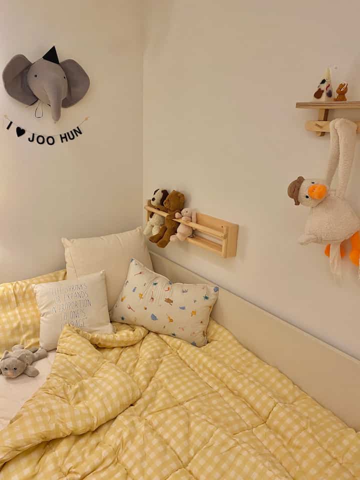 暖かいベージュと黄色のトーンの子供部屋、壁にはかわいい動物のぬいぐるみと木製の本棚が配置された居心地の良い空間