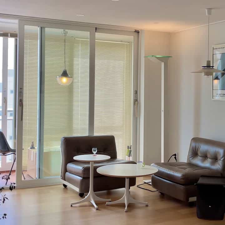 Natural modern living room with white walls and flooring, featuring brown leather sofa and round coffee tables arranged neatly