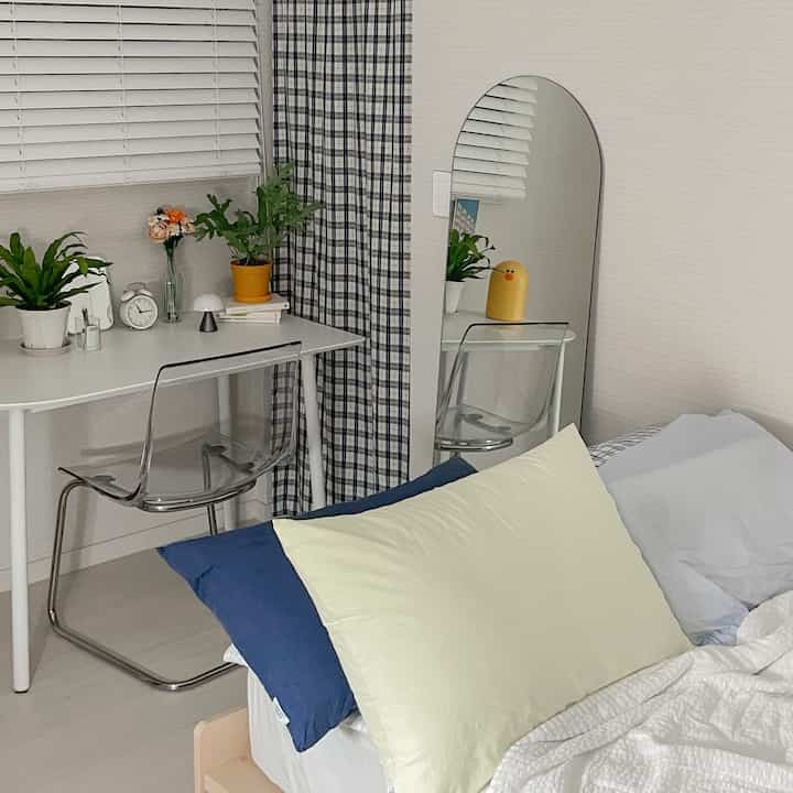 白とネイビーの色調の寝室、デスクと透明な椅子、アーチ型の全身鏡が配置された雰囲気のあるインテリア。