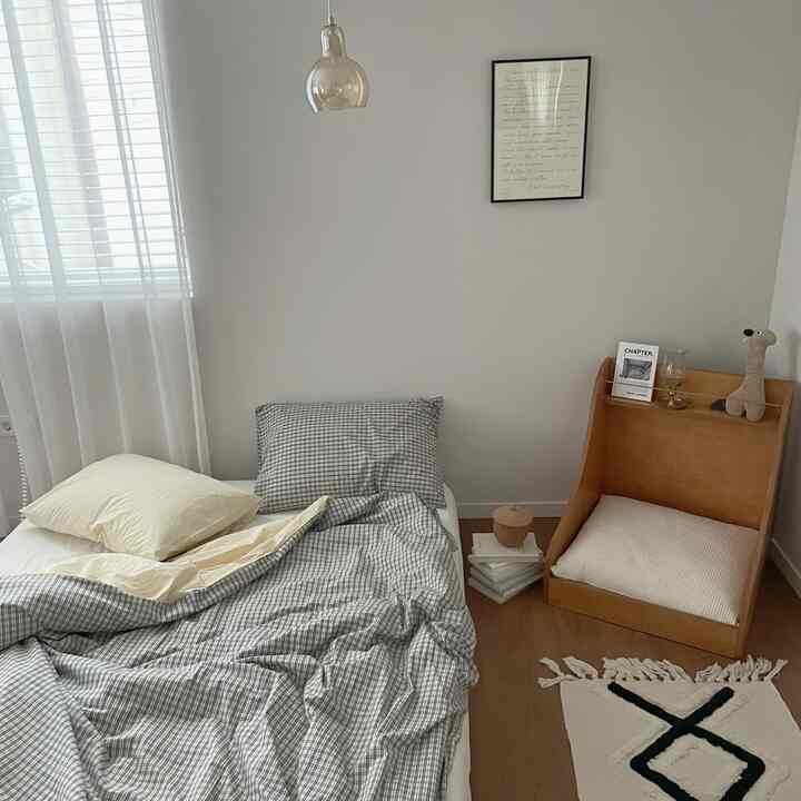 白い壁と木目調の床の一人寝室、チェック柄の寝具と枕が配置された雰囲気のある空間