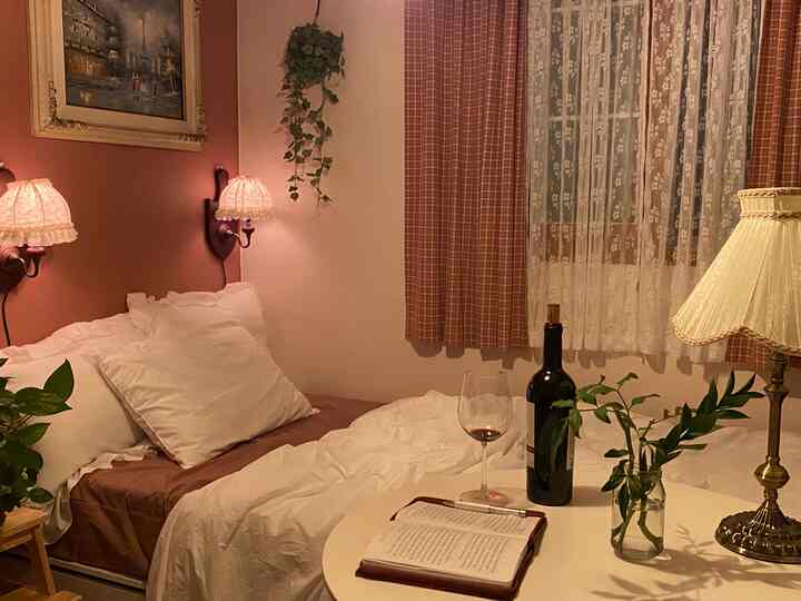 Warm beige and brown toned bedroom featuring vintage wall lamps and lace curtains, cozy space with wine and a reading diary on the table