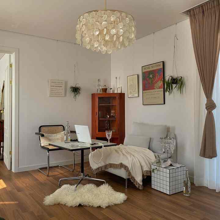 ナチュラルトーンのリビング、クリーム色のソファとアームチェア、木製の床、シャンデリア照明が配置された雰囲気のある空間