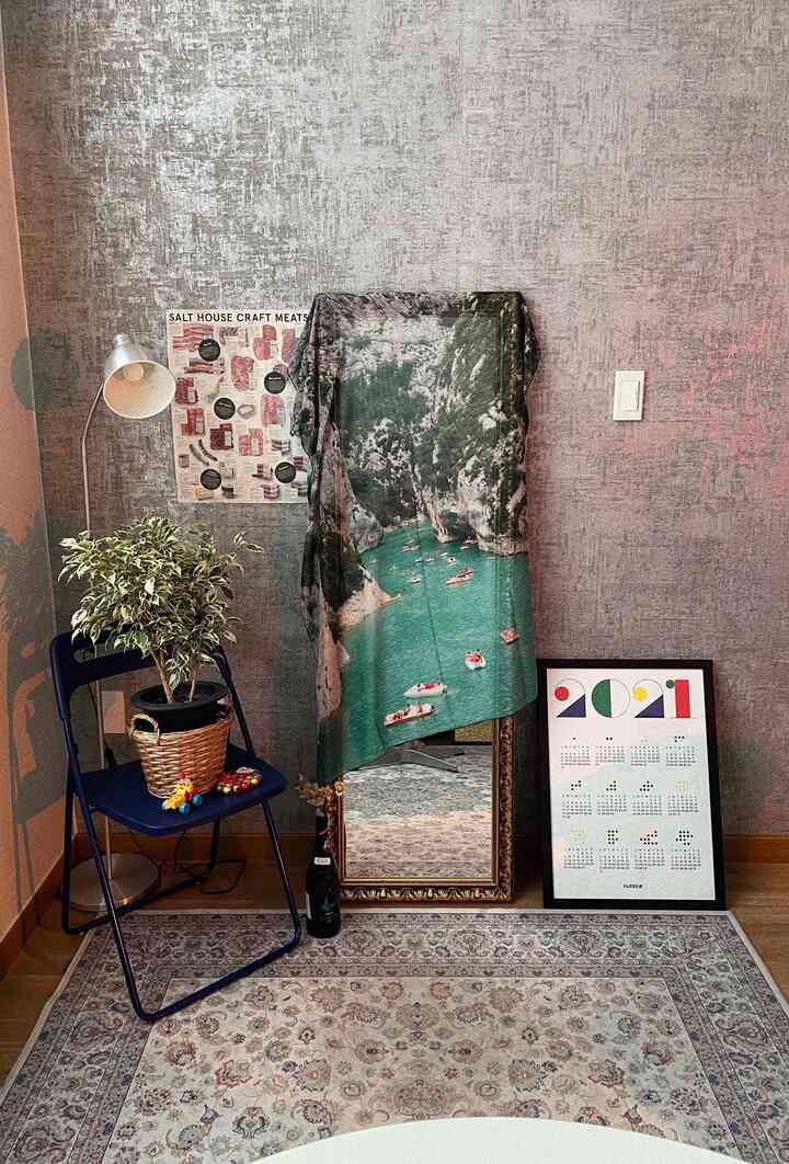 ベージュ調のラグと壁紙のある小さな空間、植物と額縁、スツール、フロアランプが配置された雰囲気のあるインテリア