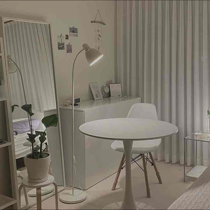 Neat white-toned room featuring a round dining table with chair, full-length mirror, and a floor lamp