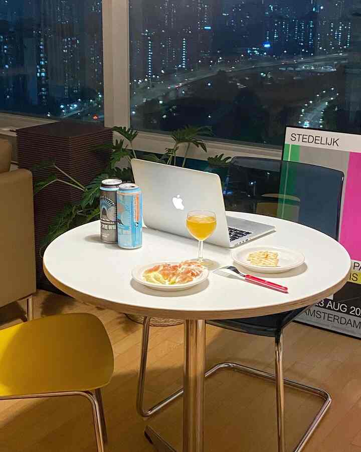 A modern and cozy dining room in white and yellow tones featuring a round dining table with beer cans, wine glass, and a MacBook for a home bar setting