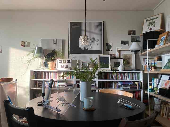 Modern living room with white walls and bookshelves filled with natural light, featuring round dining table and assorted picture frames