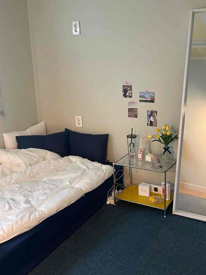 ネイビーとイエローの調和が取れた寝室、一人用ベッドとナイトテーブル、フロアミラーが配置されたシンプルな空間