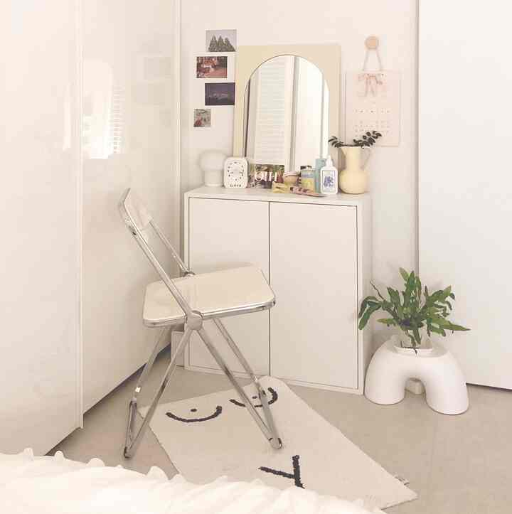 Compact room in white and ivory tones featuring IKEA EKET storage cabinet with mirror and folding chair, creating a minimal and cozy vanity space