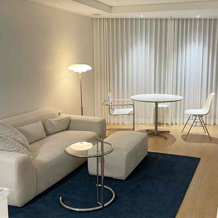 Modern living room in white and navy tones featuring a clean sofa, round dining table, side table, and floor lamp