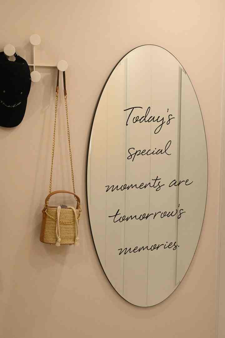 Beige-toned wall featuring an oval mirror with script and hanging hat and bag, depicting a neat closet entrance space
