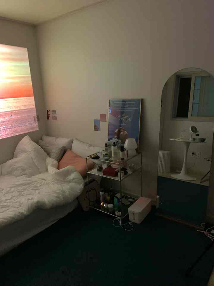 A cozy studio apartment bedroom in white and blue tones featuring a bed, multifunctional shelving unit, and a large full-length mirror