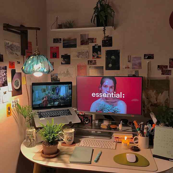 暖かいヴィンテージ照明と植物があるホームオフィス、モニターとノートパソコンが置かれた居心地の良い作業空間