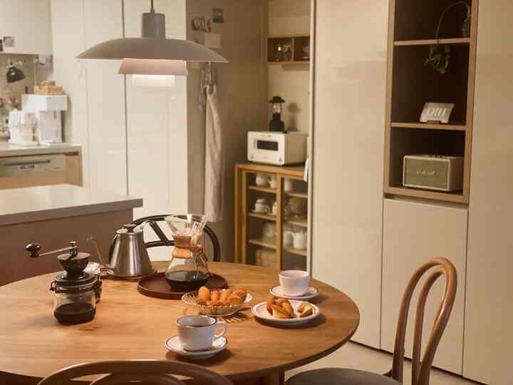 温かみのある木目調とナチュラルなベージュのキッチン、丸いダイニングテーブルを配したシンプルでおうちカフェの雰囲気ある空間