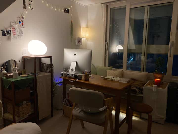 A natural wood-toned living room and home office space featuring cozy mood lighting and cushions