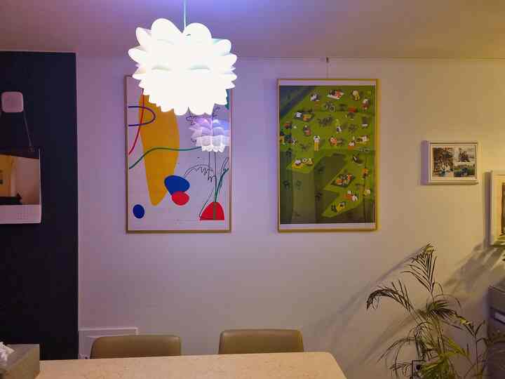 A white and beige toned kitchen featuring pendant light and two vibrant picture frames decorating the dining table wall, creating a cozy atmosphere
