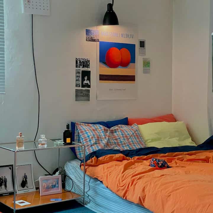 Orange and blue toned studio bedroom featuring an orange comforter and blue pillows with a cozy atmosphere