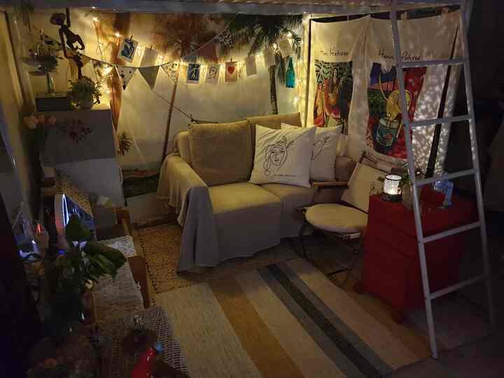 Cozy living room in warm yellow and beige tones featuring a sofa, delicate string lights, and artistic posters