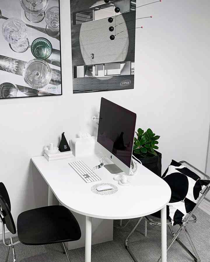 Modern home office in white and black tones featuring a rounded half-oval table, black chairs, and modern art posters on the wall creating a clean workspace