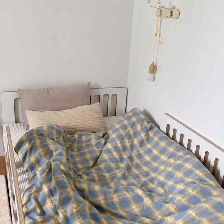 白い壁とナチュラルな木目調のベッドがあり、青と黄色のチェック柄の寝具が配置された雰囲気のある子供部屋。