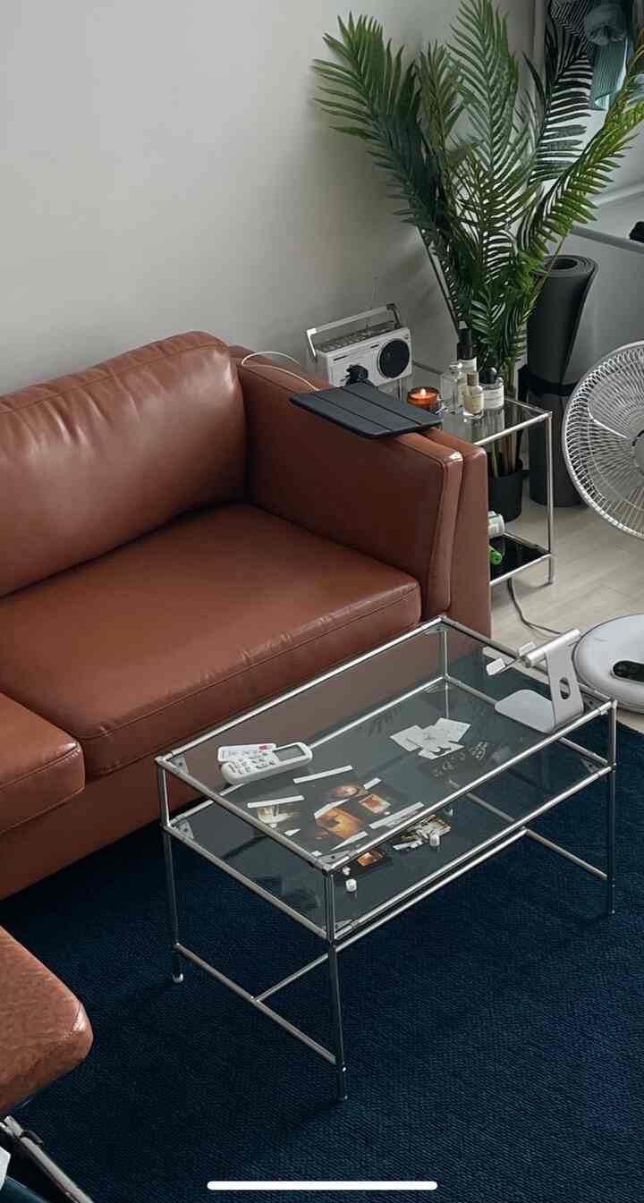 キャメル色のソファとネイビーのラグがあるシンプルなリビングルーム、メタルフレームのサイドテーブルと植物が配置された雰囲気のあるインテリア