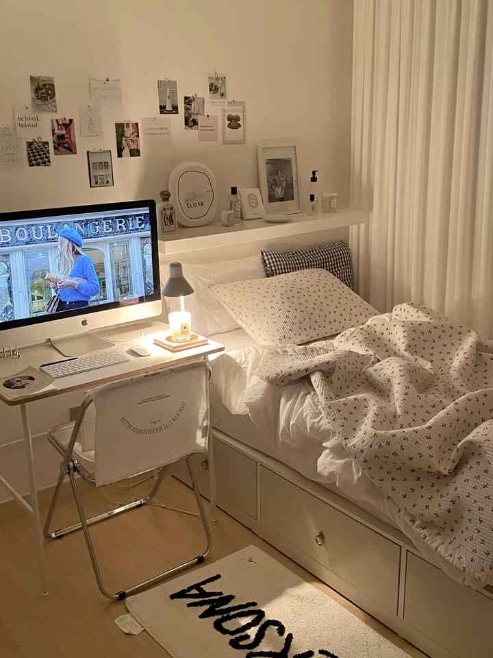 Cozy bedroom with warm white tones featuring a desk with iMac and candle, and a neatly made bed