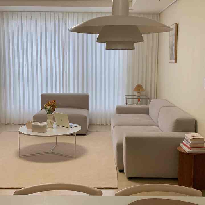 暖かみのあるベージュ色調のリビング、ベージュのソファと大きなラグ、丸い白いコーヒーテーブルが配置された落ち着いた空間