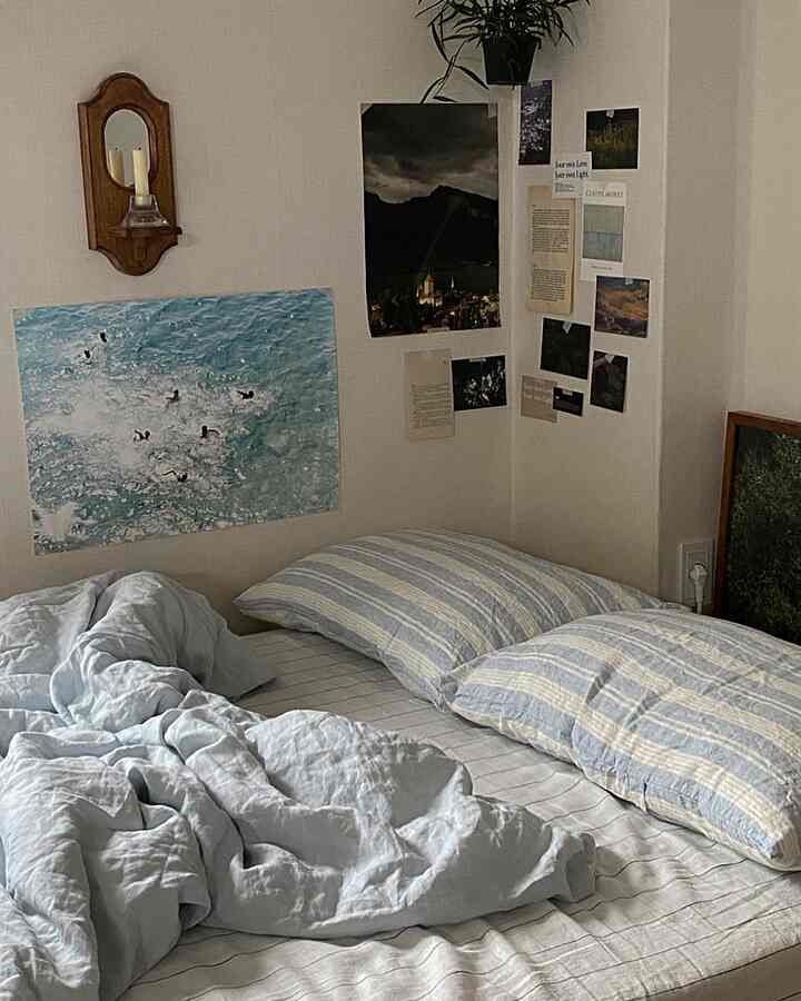 青と白のトーンのワンルーム寝室、ストライプの枕と壁のポスターが配置されたヴィンテージ感のあるインテリア