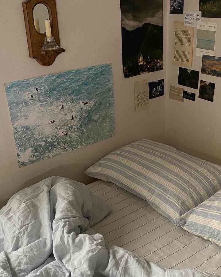 ナチュラルカラーの寝室、ストライプの枕と淡い青色の布団が置かれた雰囲気のあるヴィンテージスタイルの空間