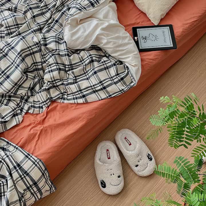 Natural warm tones in a bedroom featuring navy plaid bedding, soft linens, wooden flooring, and a green plant creating a cozy atmosphere