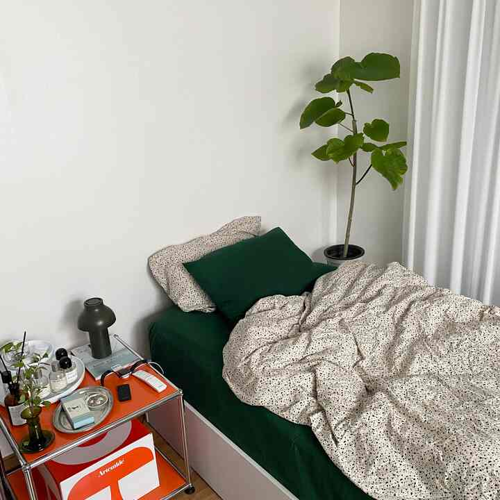 白い壁とカーテン、緑の寝具と植物が配置されたナチュラルでシンプルな寝室のインテリア