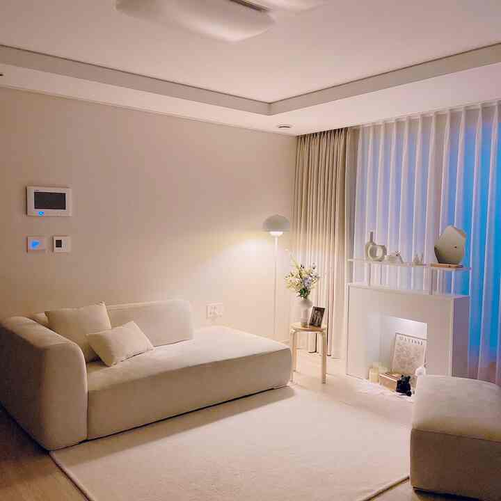 柔らかなホワイトトーンのリビング、広いソファとラグ、暖炉風のコンソールが配置されたミニマルでナチュラルな印象的な空間