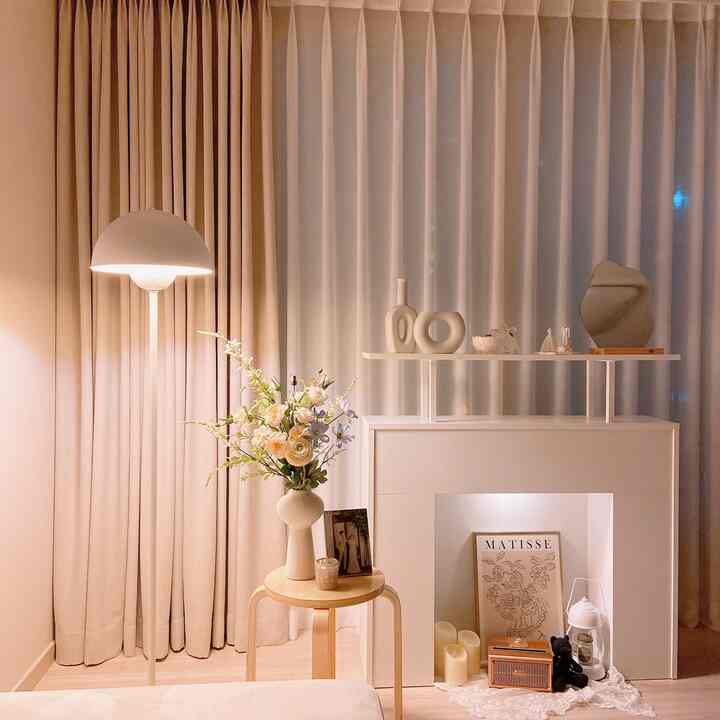 白と木目調のリビング空間、暖炉コンソールとフロアランプ、花瓶やスツールが配置された暖かな雰囲気のインテリア