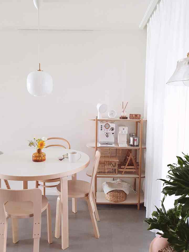 White and wood-tone kitchen featuring a round dining table and wooden shelf with coffee machines, creating a cozy home cafe atmosphere