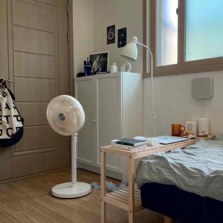 ベージュと木目調の床の寝室、白いサーキュレーターと木製のナイトテーブルが配置された落ち着いた空間